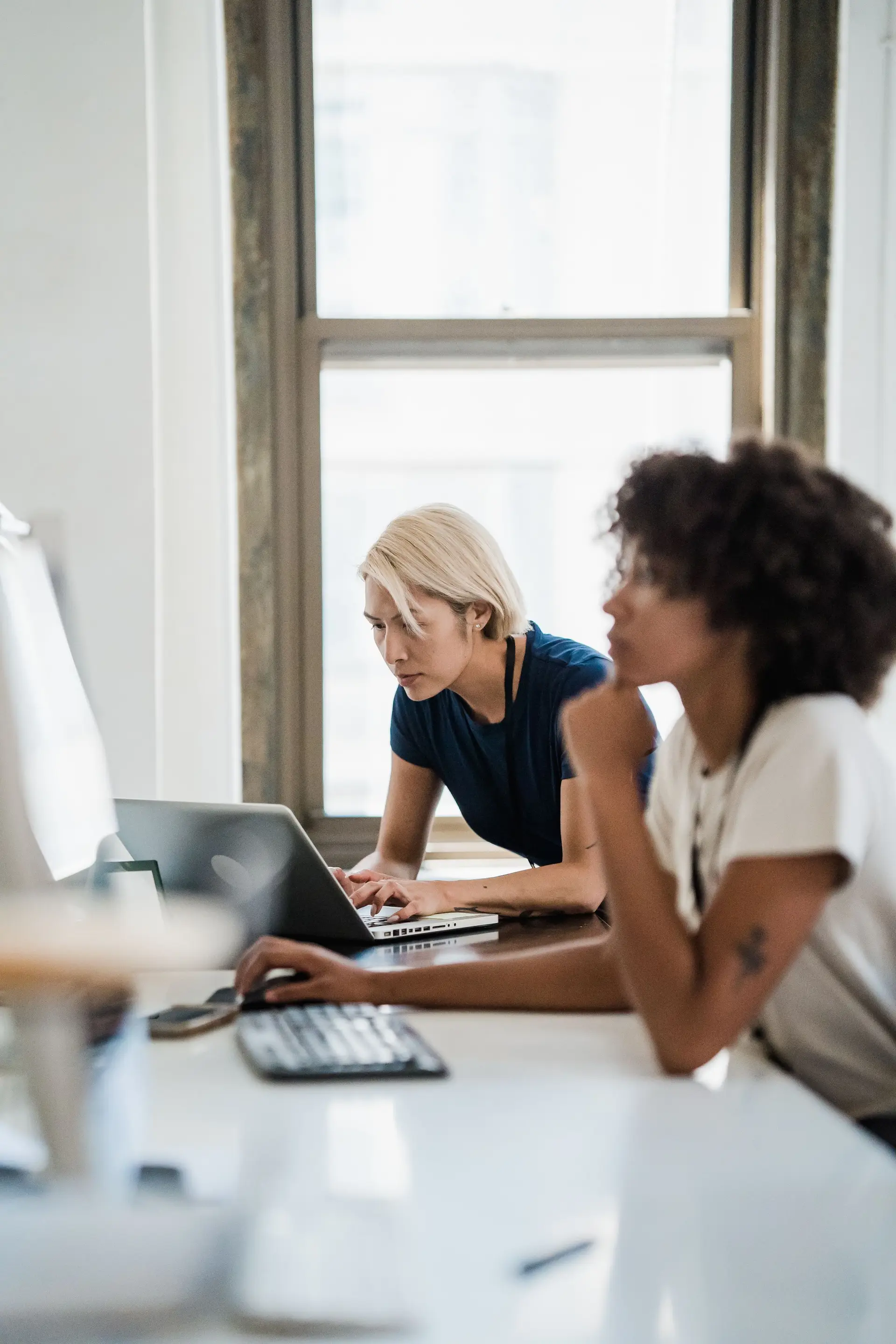 Two professionals working side by side on laptops at an office desk