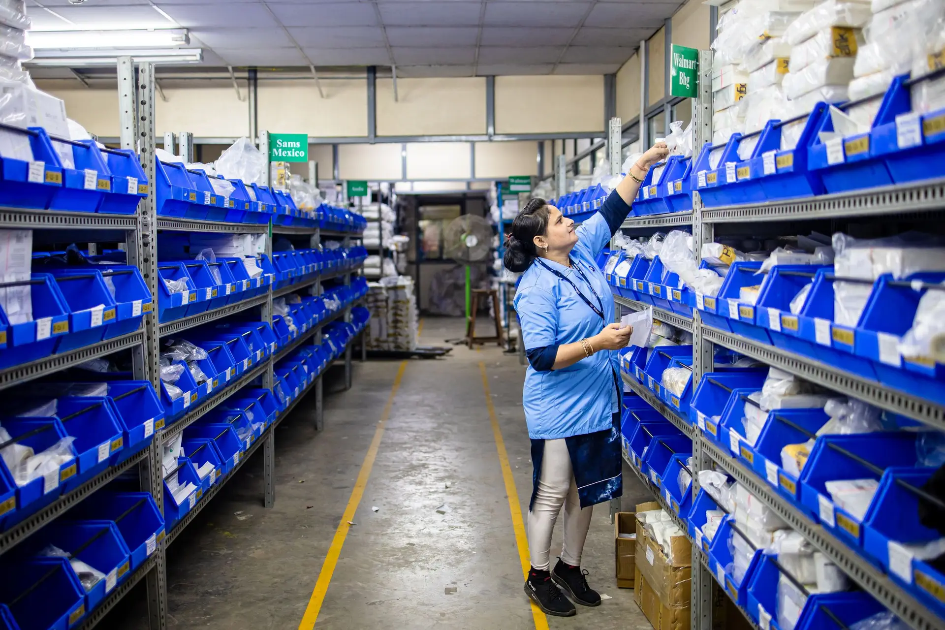 A worker organizing labelled inventory bins in a warehouse aisle